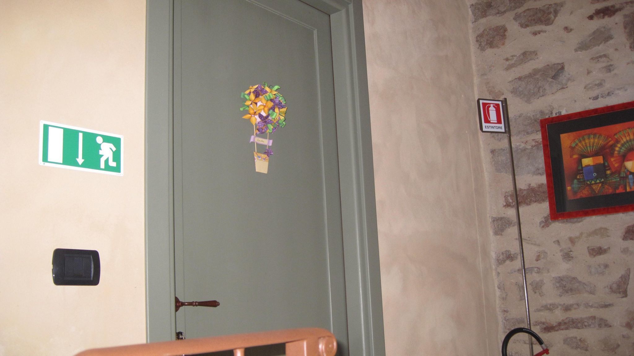 A door with a green emergency exit sign, a fire extinguisher, and a decorative hanging.