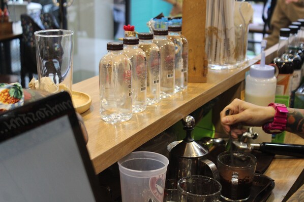 Un espace bar avec un comptoir en bois, des bouteilles transparentes et un appareil à café.