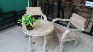 Une table ronde en bois, accompagnée de deux chaises, d’une plante en pot et d’une pancarte « BIENVENUE », le tout dans un décor de café.