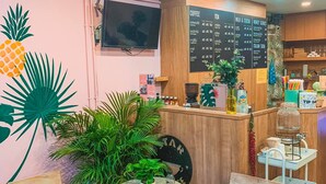 Un café chaleureux avec des meubles en bois, un tableau affichant le menu et une décoration de style tropical.