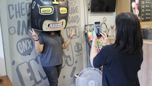 Une personne portant un masque de chat, debout devant un mur orné de divers textes et illustrations, notamment un ventilateur et un panneau de menu.