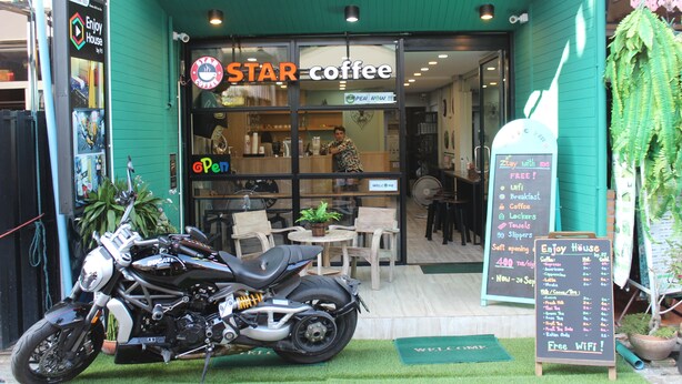 Une moto était garée devant un café, et une enseigne indiquait : « Savourez nos spécialités ».