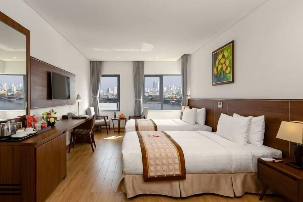 A hotel room with two beds, a desk with a chair, a TV, and a city view.