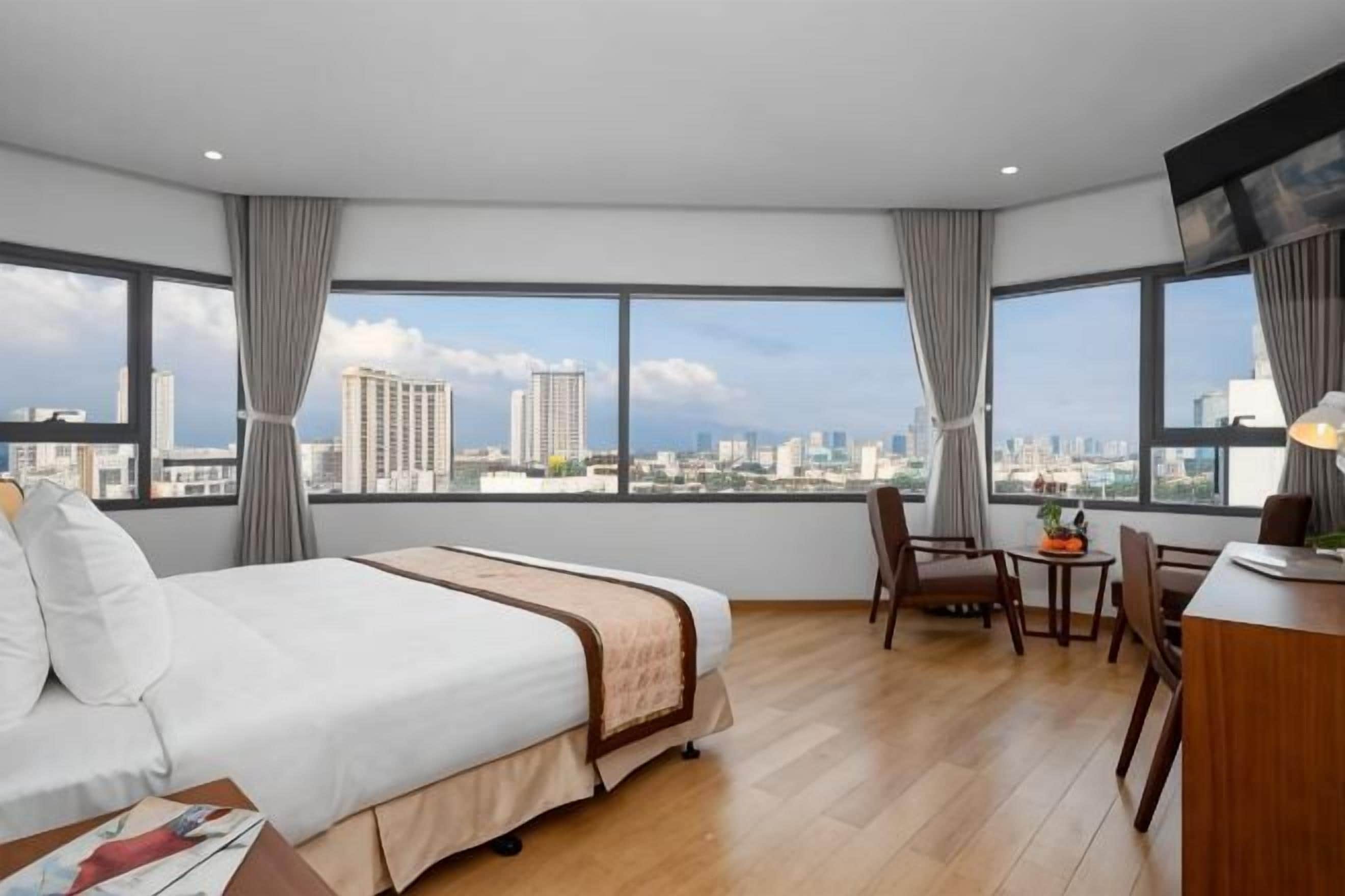 A hotel room with a large bed, a desk, a chair, and a view of the city.