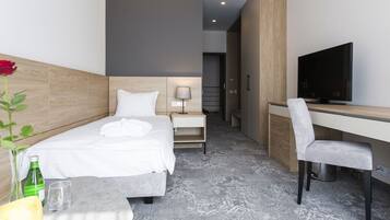 A modern hotel room with a bed, a desk, a chair, a television, and a small table with a glass and a bottle.
