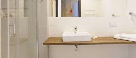 Un baño moderno con cabina de ducha de vidrio, tocador de madera y lavamanos blanco.