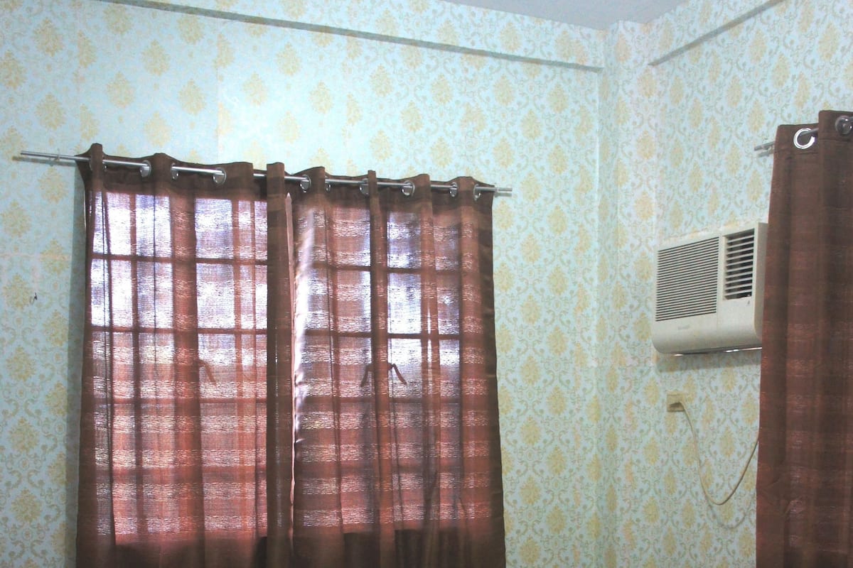 A room with a bed, curtains, an air conditioning unit, and a patterned wall.