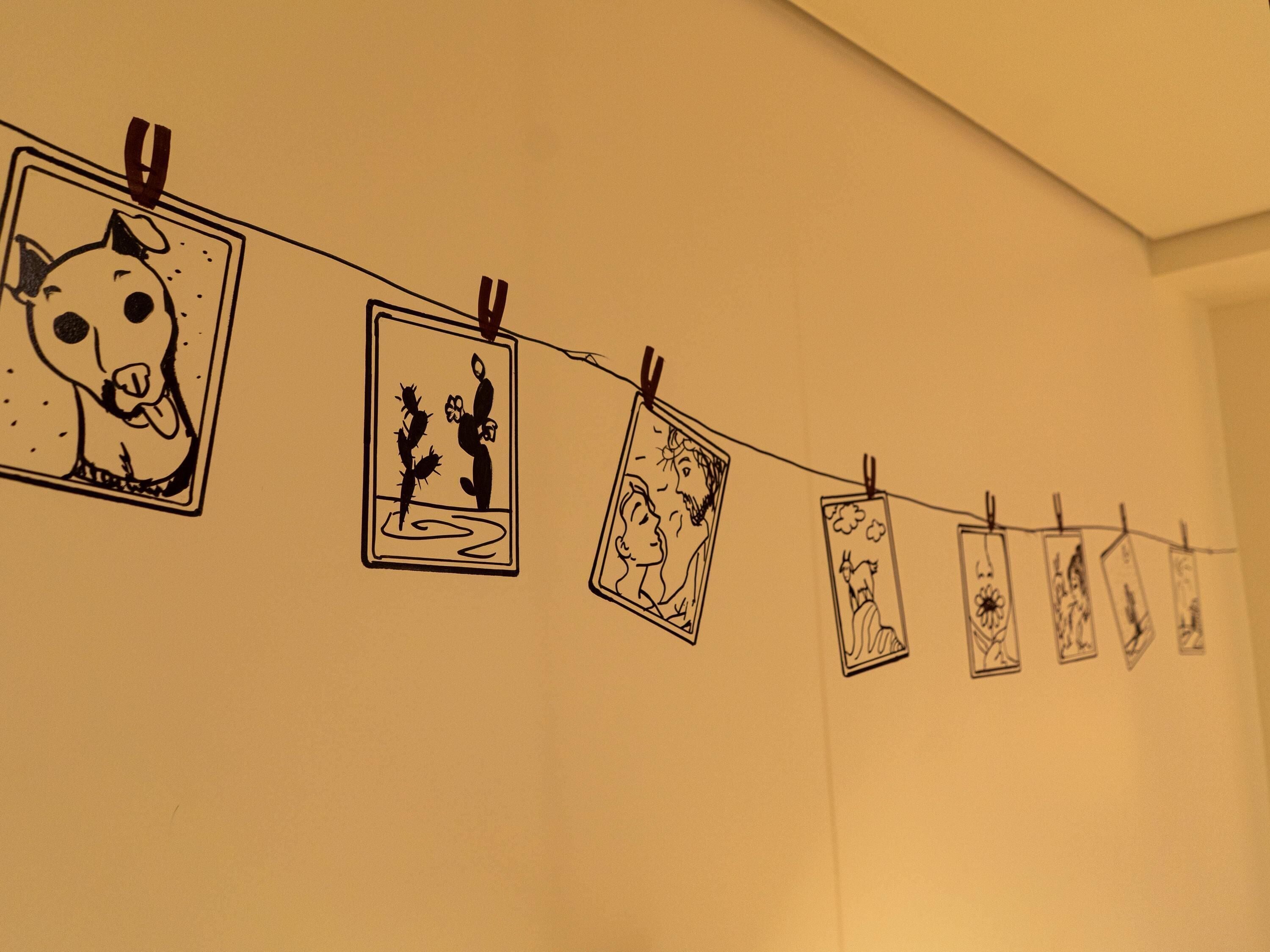 A wall with a series of square drawings clipped to a string.