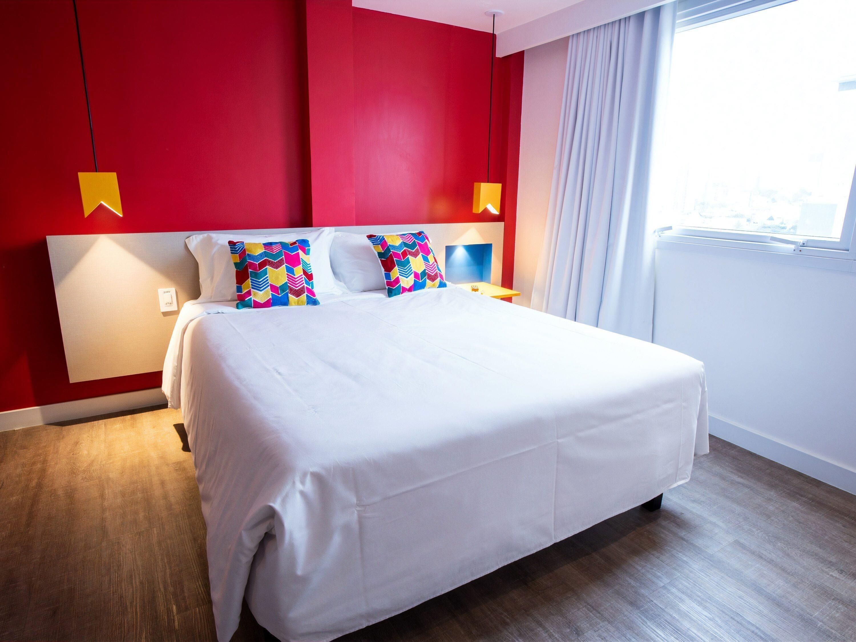 Een hotelkamer met een groot bed, rode wanden en uitzicht op de stad.