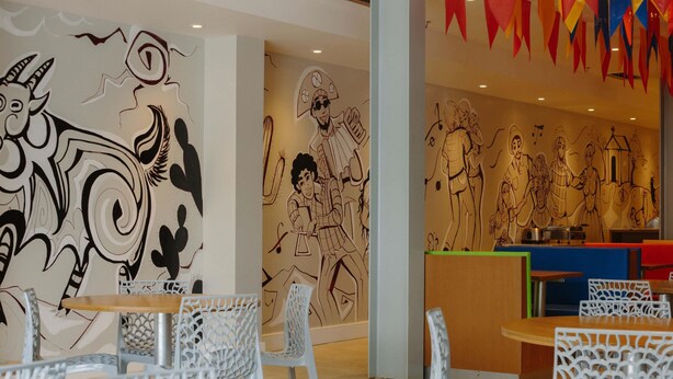 A restaurant with white chairs, a wooden table, and walls decorated with black and white murals.