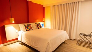 A hotel room with a bed, a chair, a curtain, and a wall with a light fixture.