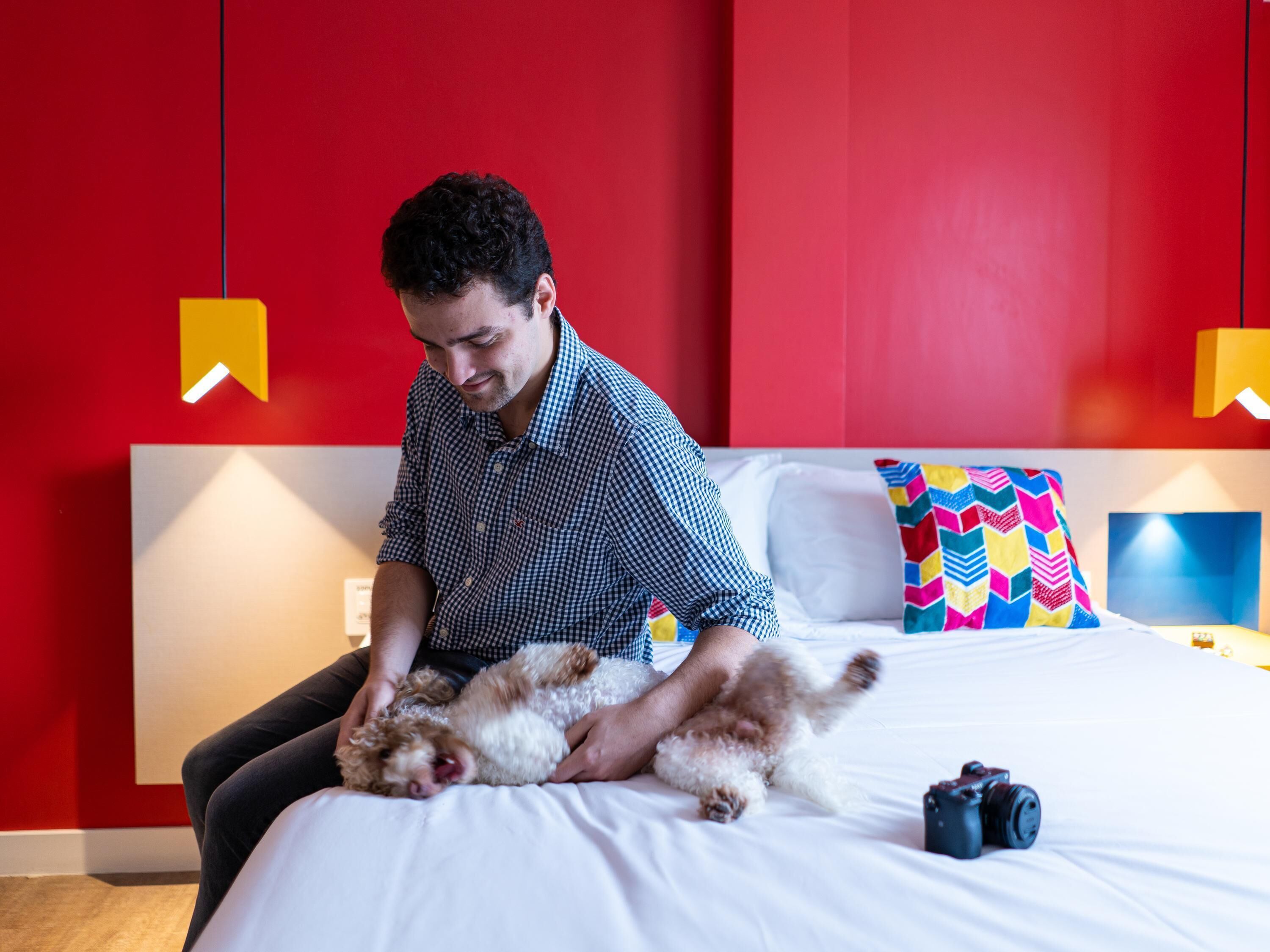 A man sitting on a bed with a small dog, holding the dog.