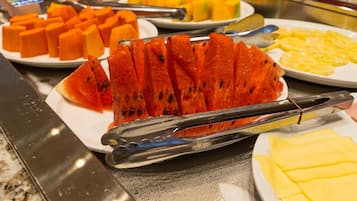Un bufé con diversas frutas y verduras, incluyendo sandía y piña, dispuestas en platos.