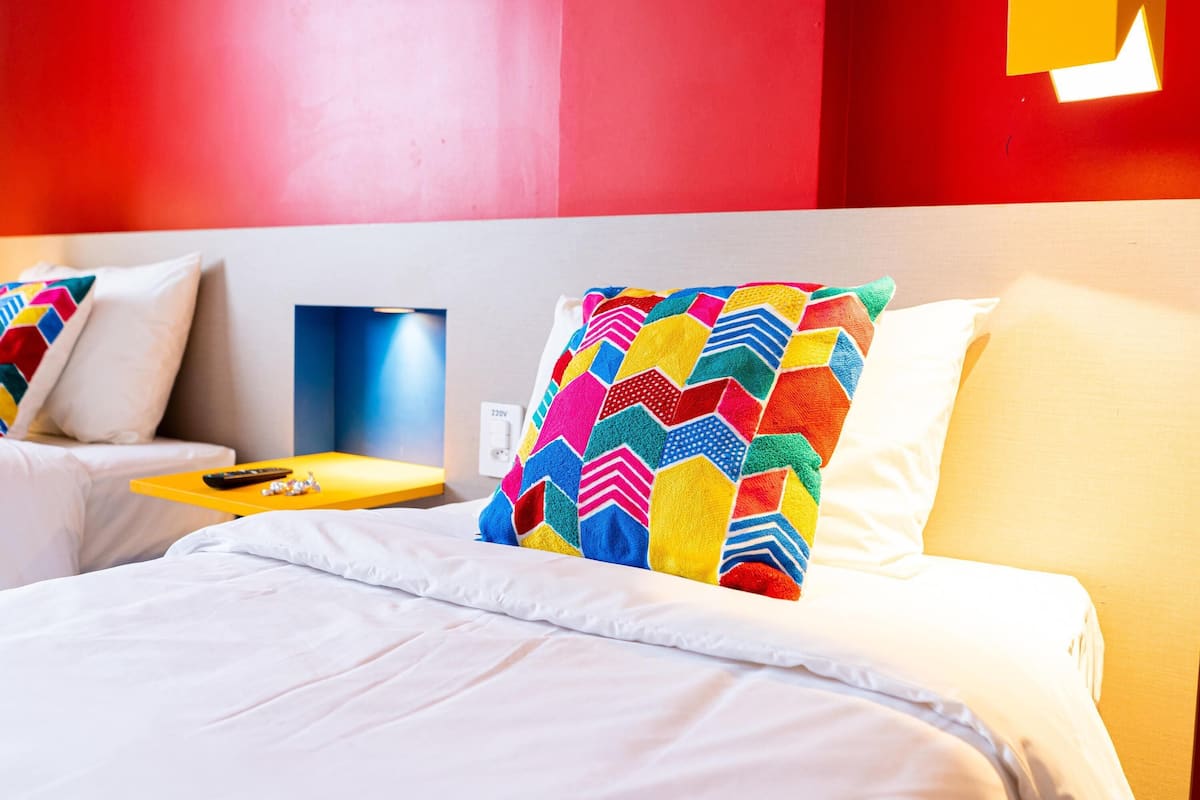 Une chambre d’hôtel comprenant un lit, une table de chevet, une lampe et un luminaire fixé au mur.