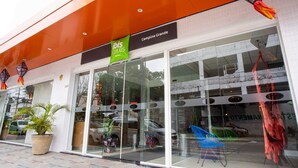 A hotel entrance with a glass facade, a green sign above the entrance, and decorative hanging lanterns.
