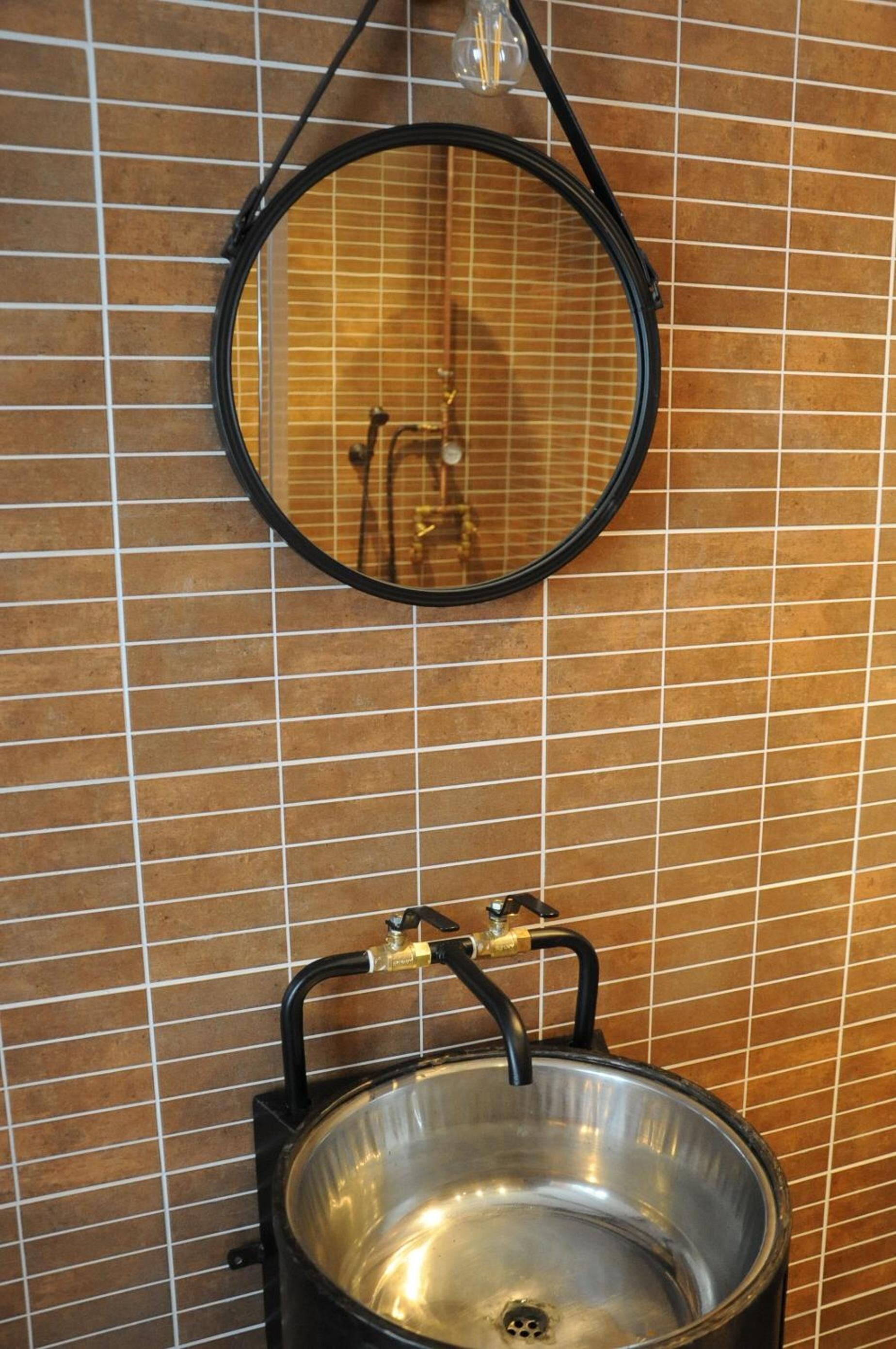 Een badkamer met een ronde spiegel en een roestvrijstalen wastafel op een betegelde muur.