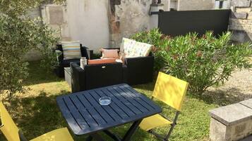 An outdoor seating area with a table and chairs, a sofa, and a small garden with plants and a wall.