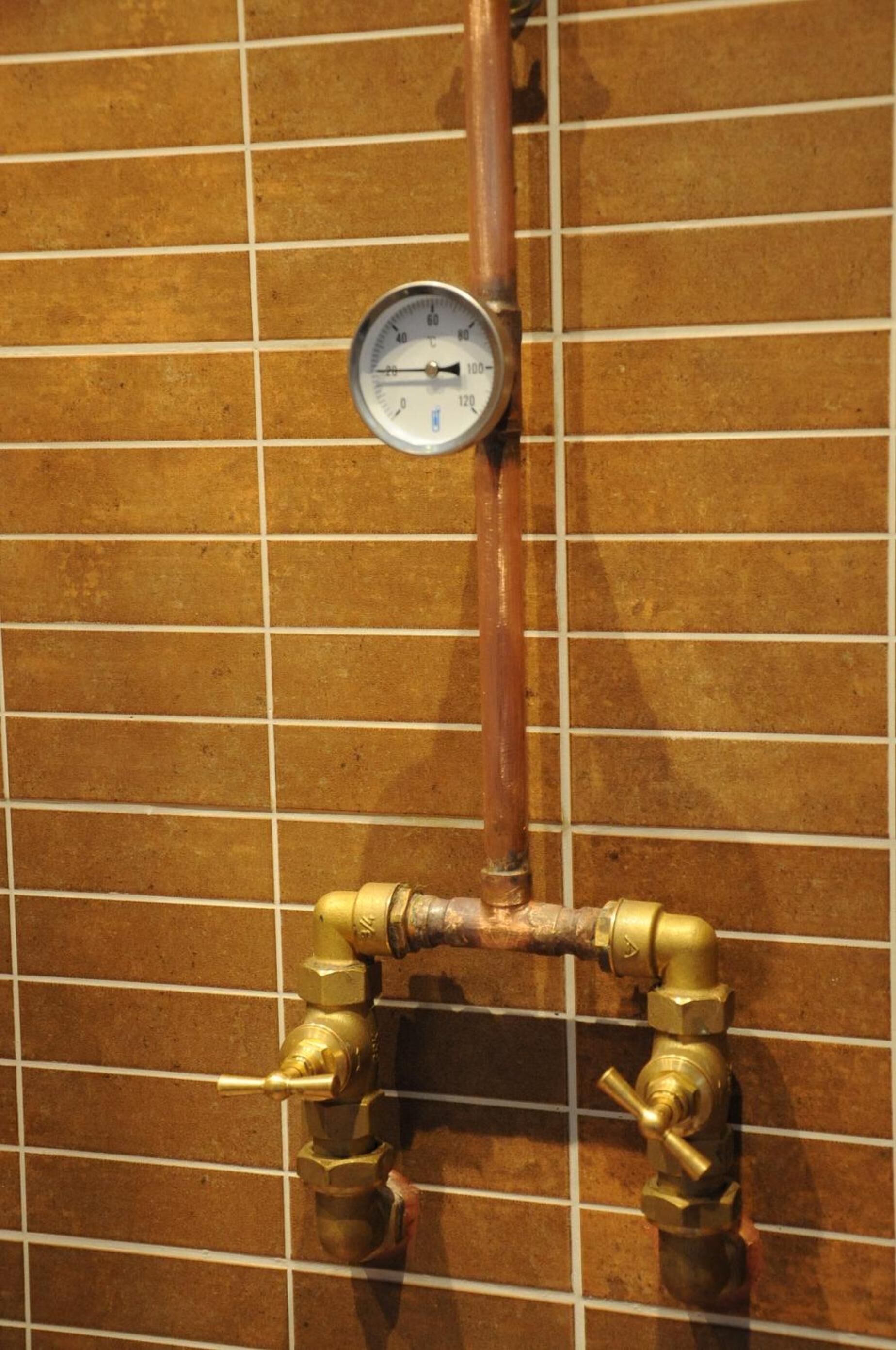 Un baño con pared de azulejos, un manómetro y accesorios de latón.