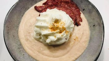 Un plato con una crema suave, una cucharada de crema agria y un trozo de carne roja sobre un plato oscuro.