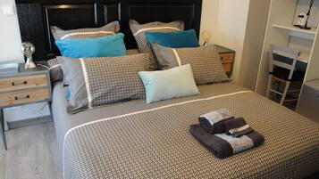 Une chambre à coucher bien rangée, avec une couvre-lit à motifs, plusieurs coussins, une table de chevet avec une lampe et une chaise.