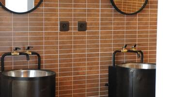 A bathroom with two sinks, each with a large metal container, a mirror, and a wall-mounted light fixture.