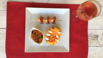 Un plato blanco con brochetas, melón y salsa sobre un tapete rojo.