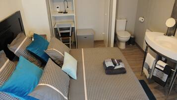 Une chambre compacte comprenant un lit, des tables de chevet, un bureau, une armoire, des toilettes et une salle de bain avec un lavabo et un miroir.