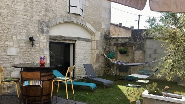 Un patio exterior con muro de piedra, una mesa de barril de madera, sillones, una hamaca y un pequeño elemento acuático.
