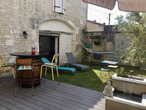 Eine Terrasse im Freien mit einer Steinsäule, einem Holzbartisch, Lounge-Stühlen, einer Hängematte und einem kleinen Wasserspiel.