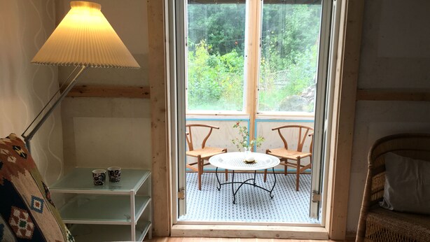A cozy room with a bed, a small table with a cup, a chair, and a lamp. - Lille Carlsson Studio (Broby)