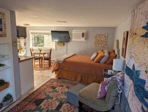 A bedroom with a bed, a desk, a chair, a TV, and a window.