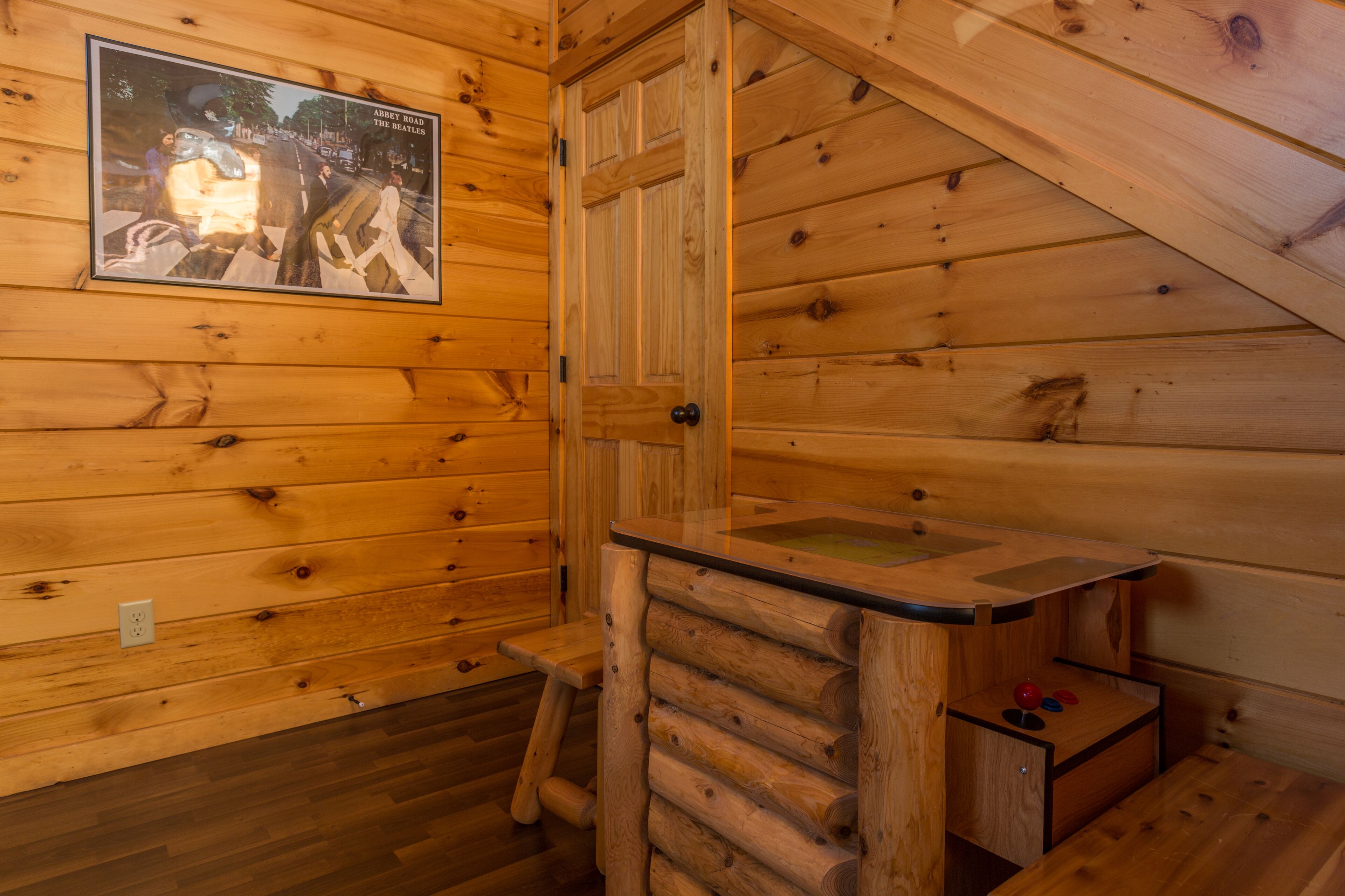 A wooden cabin interior with a wooden door, a small table, and a poster on the wall.