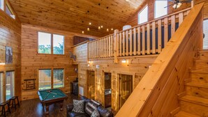 A wooden cabin interior with a pool table, leather sofa, and a staircase leading to a loft area. - The Game Changer! Next to Dollywood/Hot-Tub/Pool/LUXURY (Pigeon Forge)