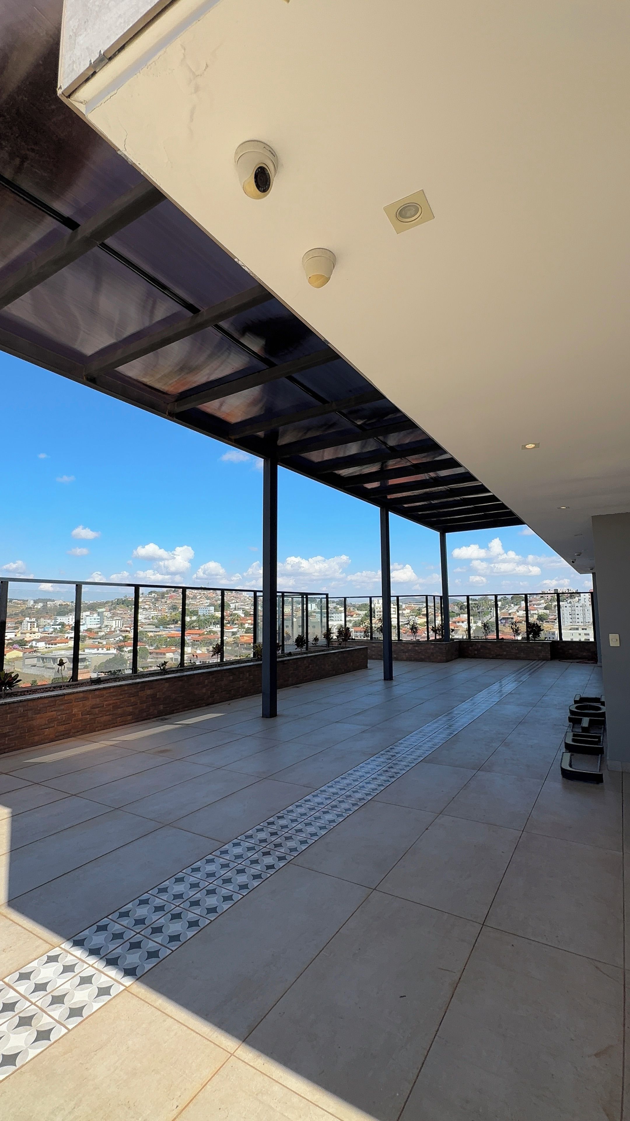 Una terraza abierta con vistas a un paisaje urbano, con suelo de baldosas y barandilla de metal.