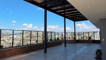 Una terraza abierta con vistas a un paisaje urbano, con suelo de baldosas y barandilla de metal.