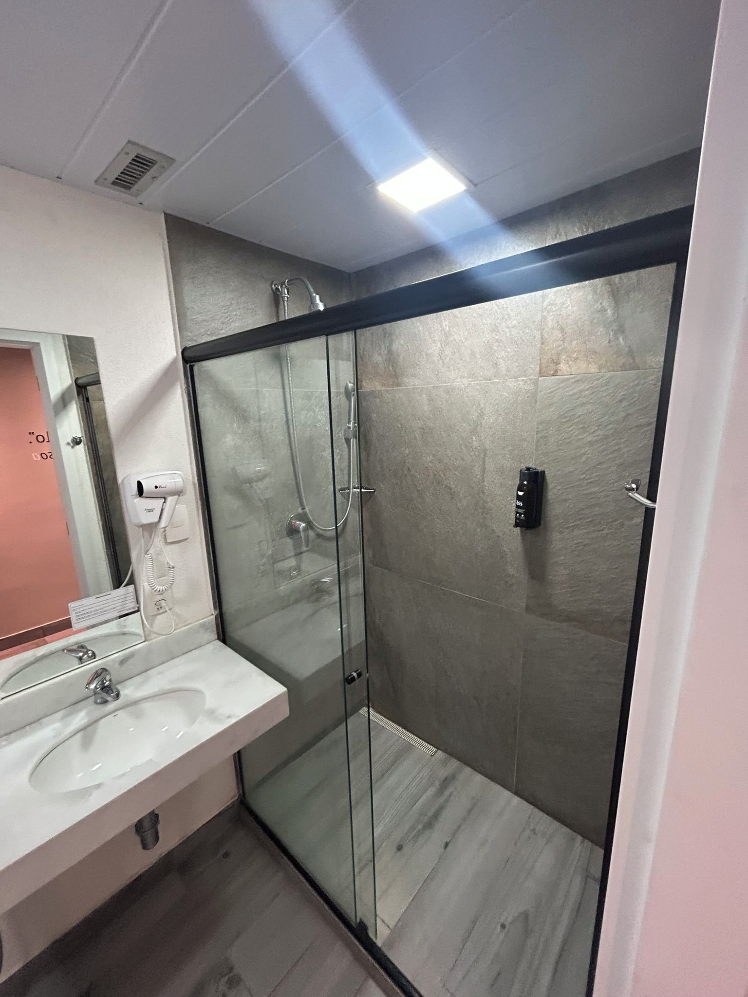 A modern bathroom with a glass shower enclosure, a white sink, and a mirror.