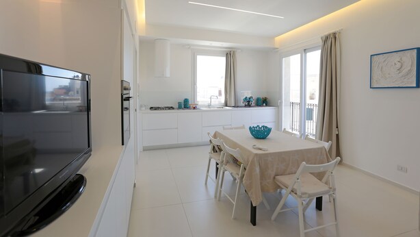 A modern kitchen with a dining area, a flat-screen TV, and a large window. - Appartamento Agamennone (Ragusa)
