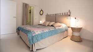 A neatly made bed with a floral bedspread, a bedside lamp, and a wicker side table. - Appartamento Agamennone (Ragusa)