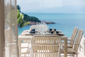 A dining table set with glasses and plates, overlooking a coastal view. - Samui Bayside Luxury Villas (Koh Samui)