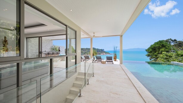 Un área exterior moderna con barandilla de vidrio, piscina y vista al mar.