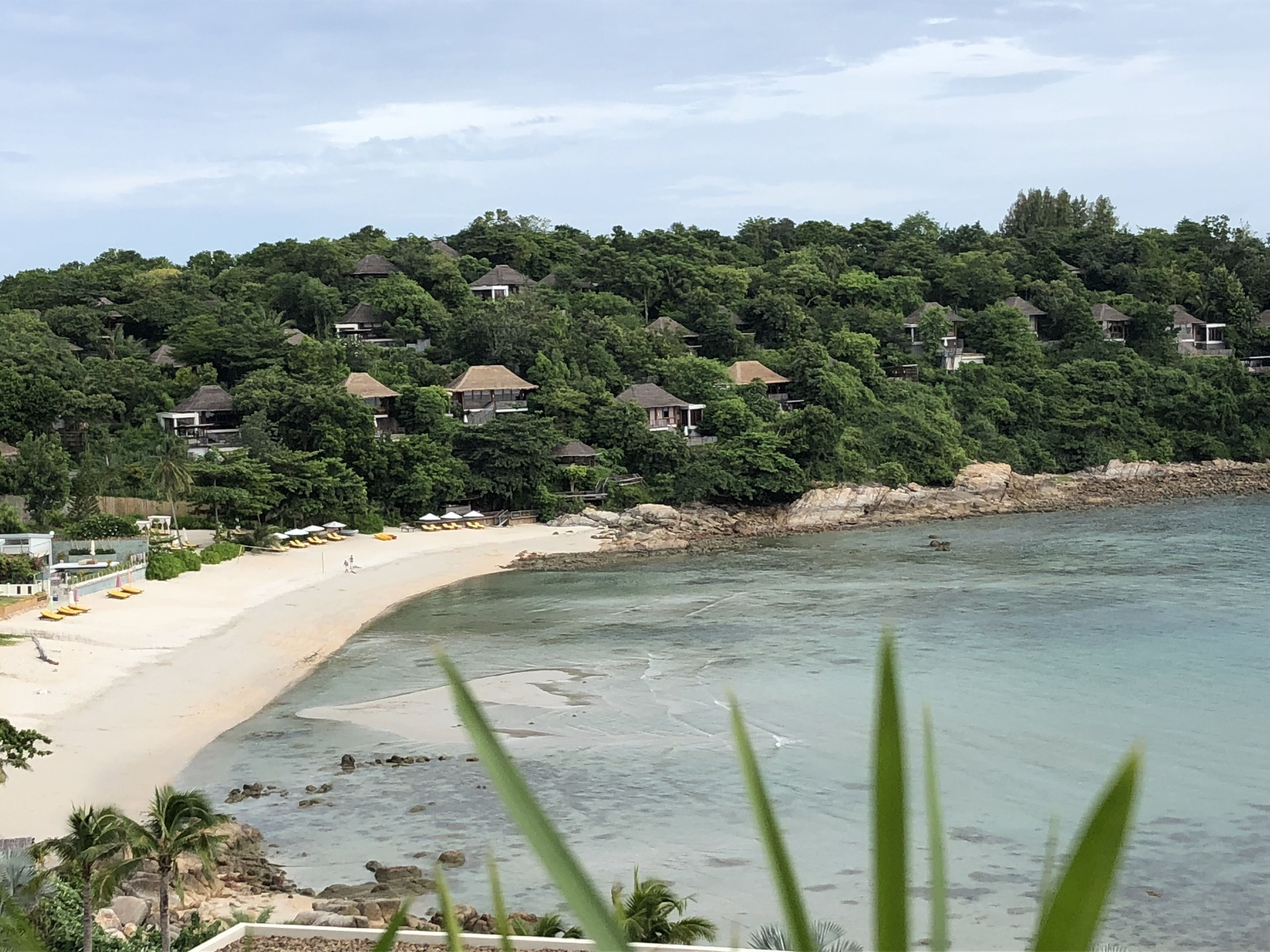 Una playa con una hilera de casas en una colina, arena y agua cristalina.