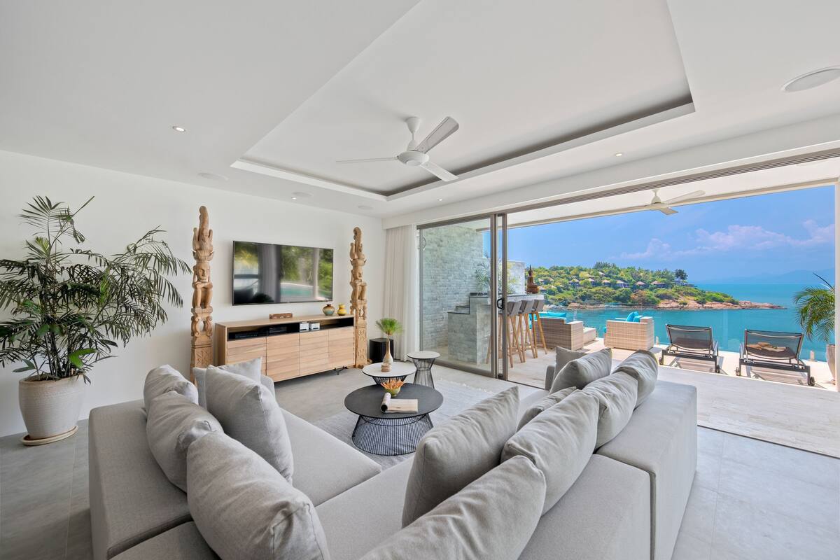 Una sala de estar moderna con un sofá grande, un televisor y vistas a un paisaje costero.