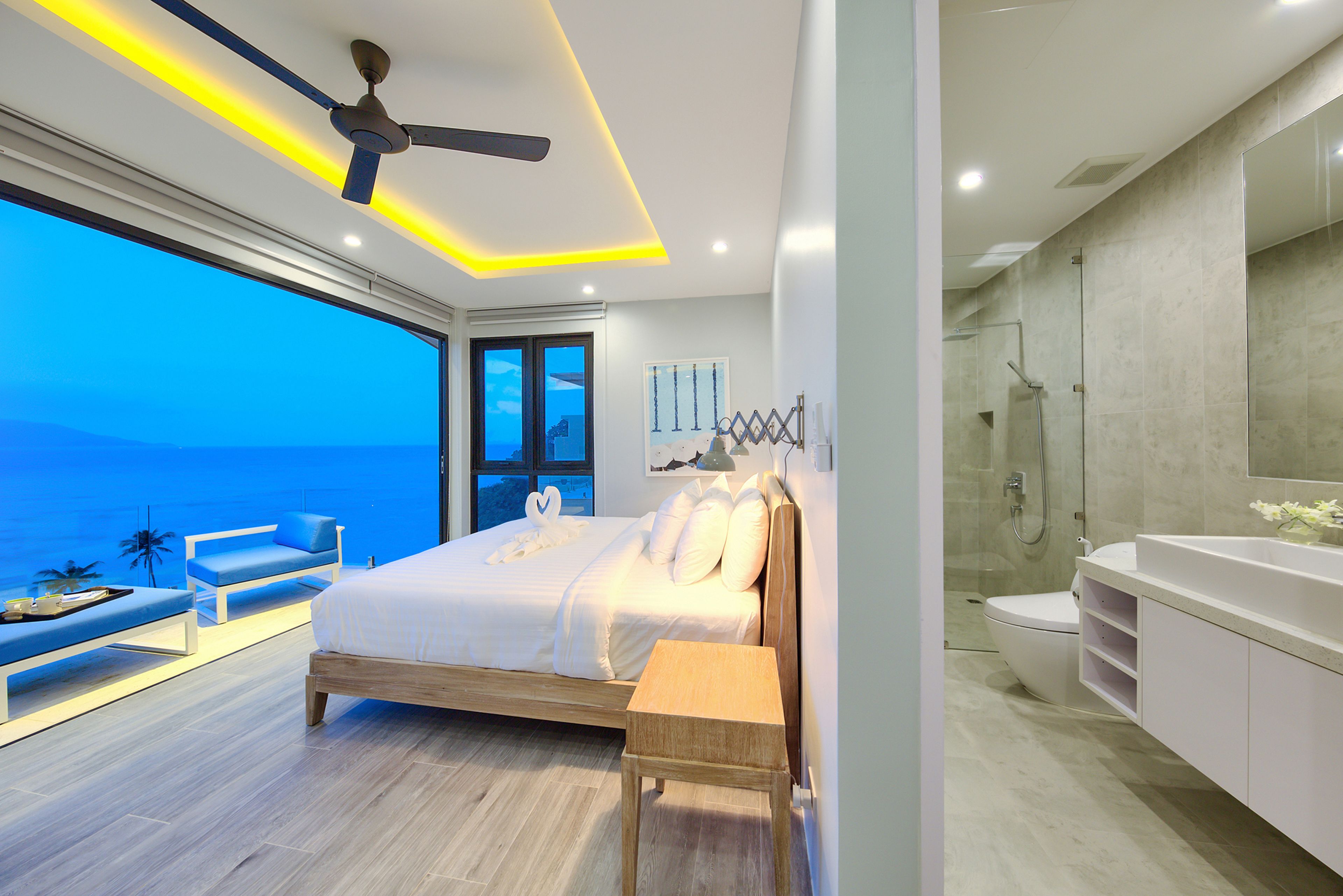 Une chambre moderne avec un grand lit, un ventilateur de plafond et une vue sur l’océan.