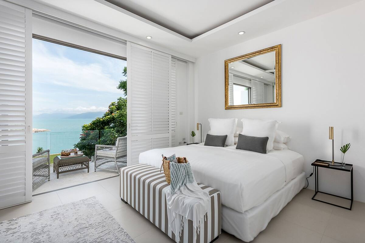 Un dormitorio moderno con una cama grande, una mesita de noche, una silla y vistas al océano.
