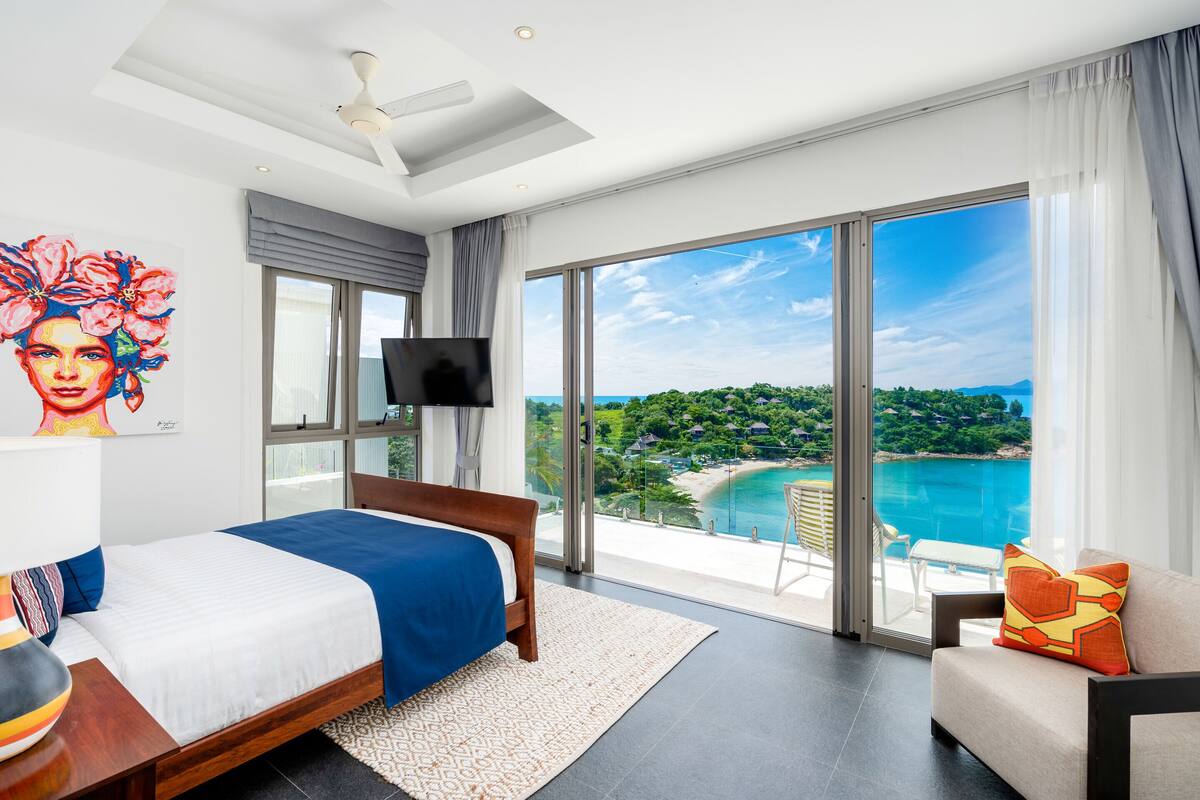 Habitación de hotel moderna con una cama grande, televisión y balcón con vistas a una playa y al océano.