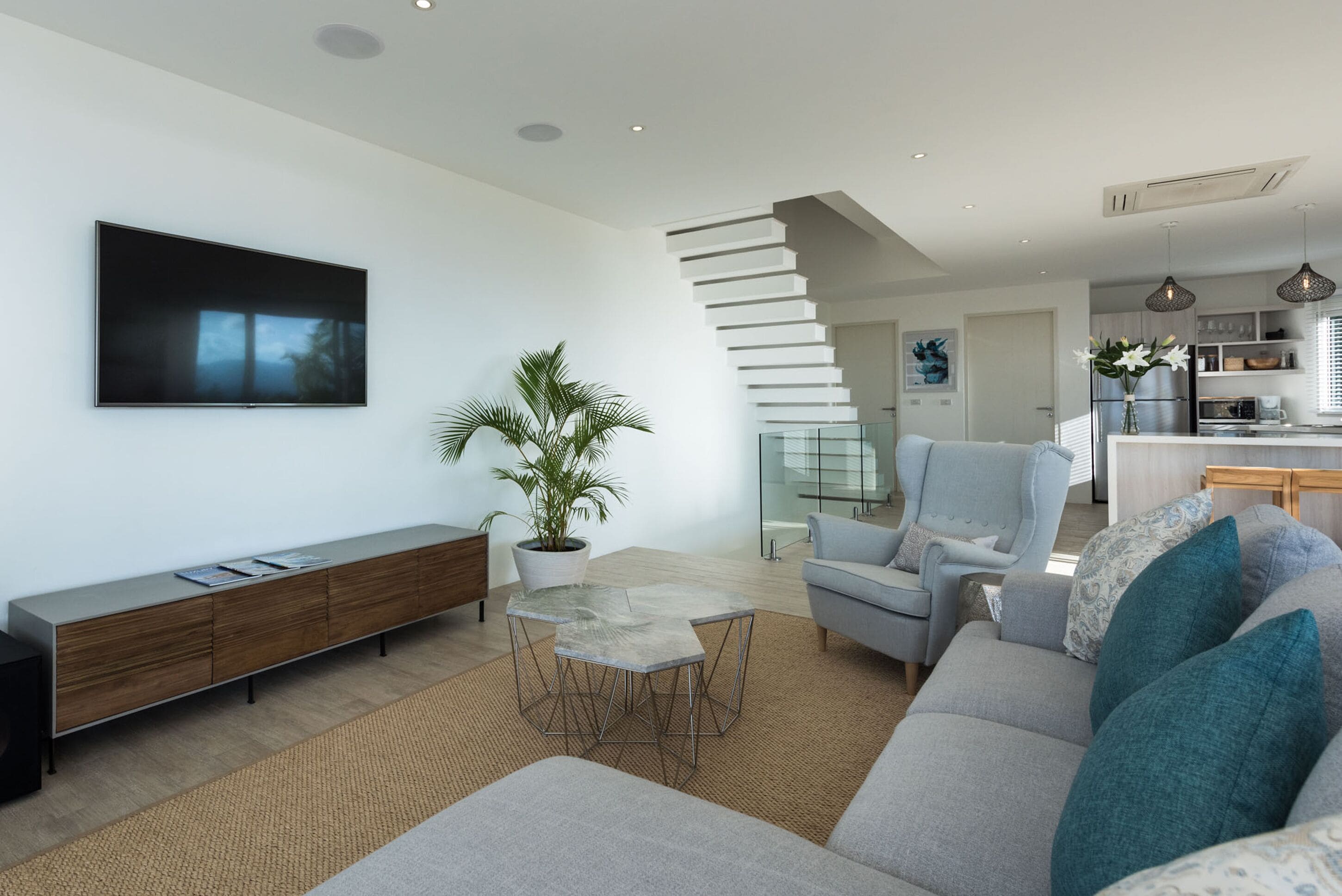 A modern living room with a flat-screen TV, a potted plant, a light blue armchair, and a grey sofa.