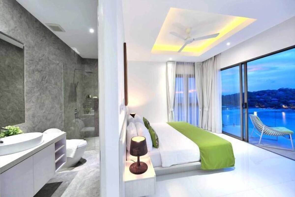 Un dormitorio moderno con un ventanal grande, una cama, una mesita de noche y un baño con ducha.