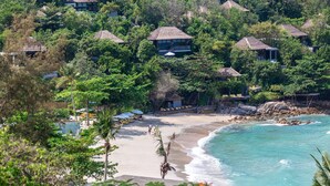 Una propiedad frente a la playa con varias cabañas sobre el agua, rodeada de exuberante vegetación y una playa de arena.