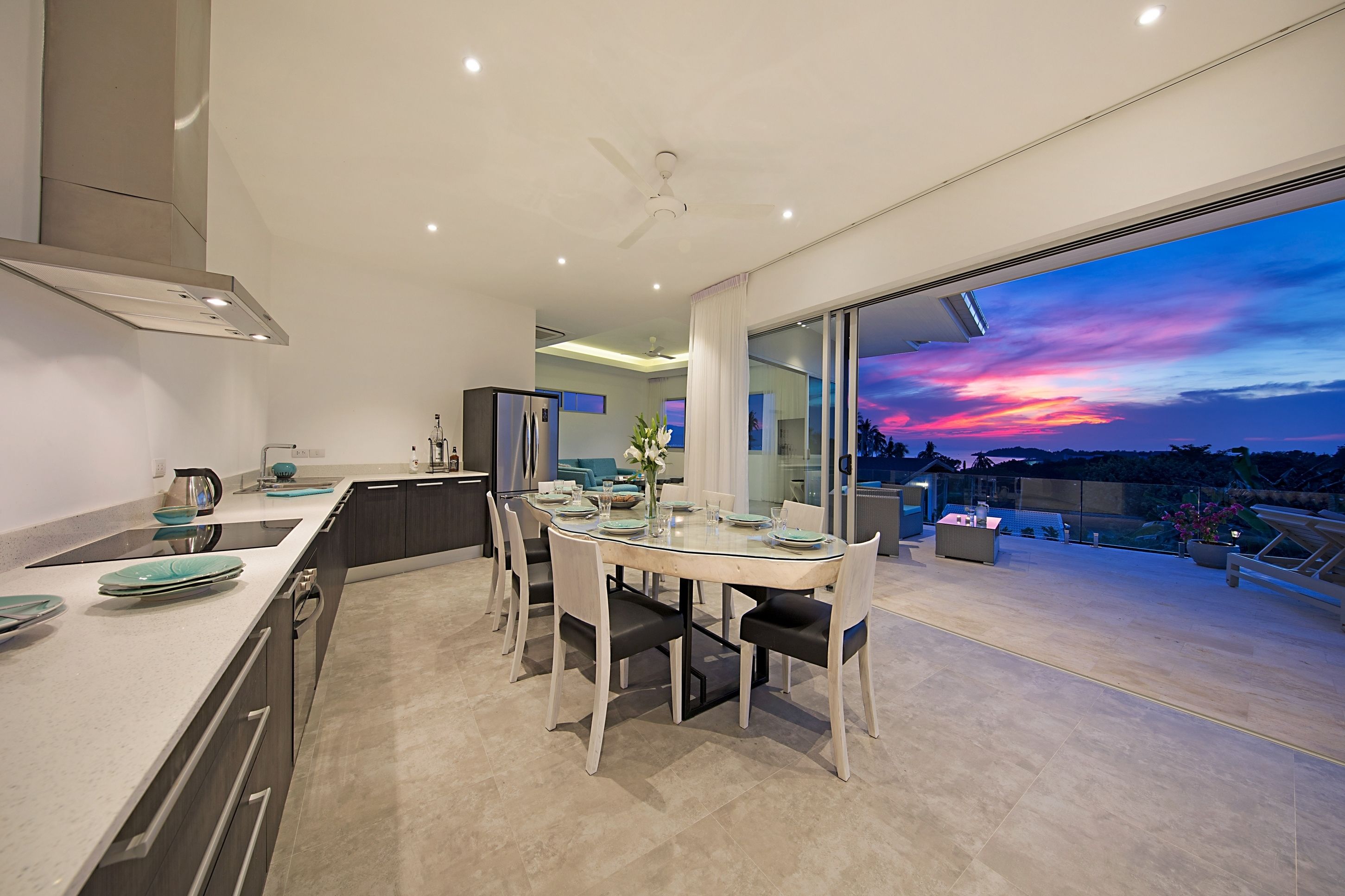 A modern kitchen with a dining area, large windows, and a view of the sky.