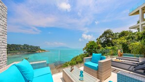 Una terraza con mobiliario de mimbre, una mesa de vidrio y vista al mar.